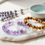 Amethyst, moonstone and tiger's eye crystal bead bracelets resting on a selenite charging slab beside a bowl of water and dried lavender, flat-lay in soft natural light