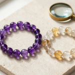 Two crystal bead bracelets on a slate slab beside a jeweler's loupe, showing natural inclusions vs glass bubbles