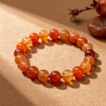 Handmade fire element crystal bead bracelet with carnelian, amber and red jasper beads, flat-lay on warm terracotta linen