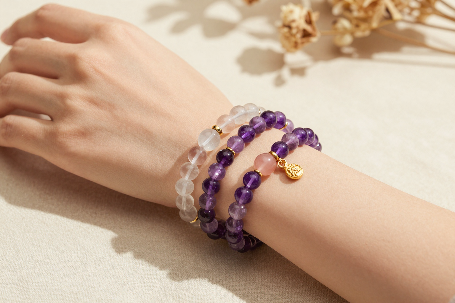 Woman's wrist wearing stacked amethyst, clear quartz and rose quartz beaded bracelets