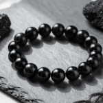 Black obsidian bead bracelet with glossy volcanic glass beads, flat-lay on slate linen