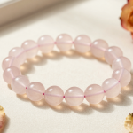 Rose quartz bead bracelet in soft blush pink, flat-lay on cream linen with dried rose petals