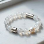 Handmade metal element crystal bead bracelet with clear quartz, white agate and a freshwater pearl with brushed silver accents, flat-lay on pale grey marble