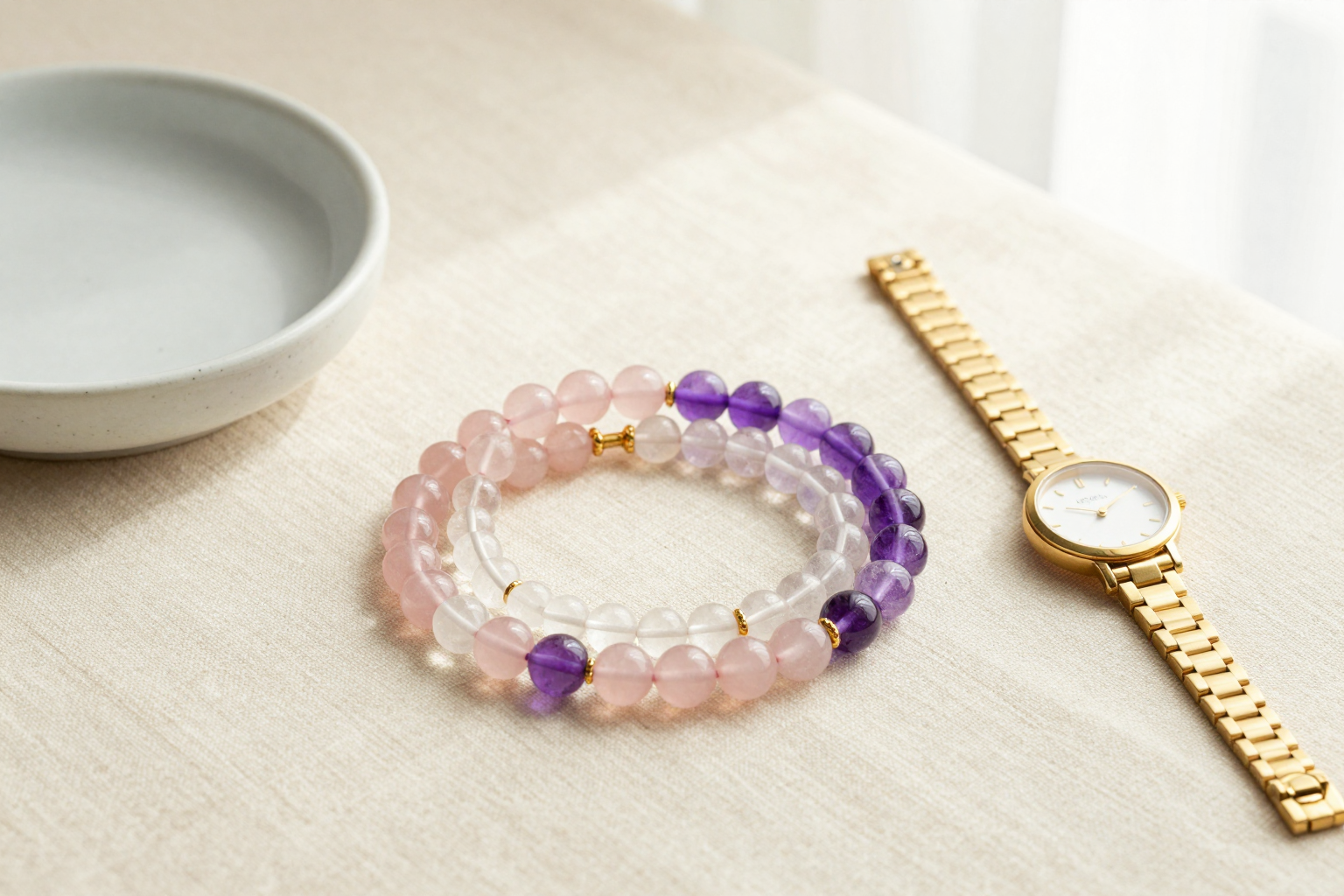 Rose quartz, clear quartz and amethyst crystal bead bracelets in a flat-lay beside a slim gold watch