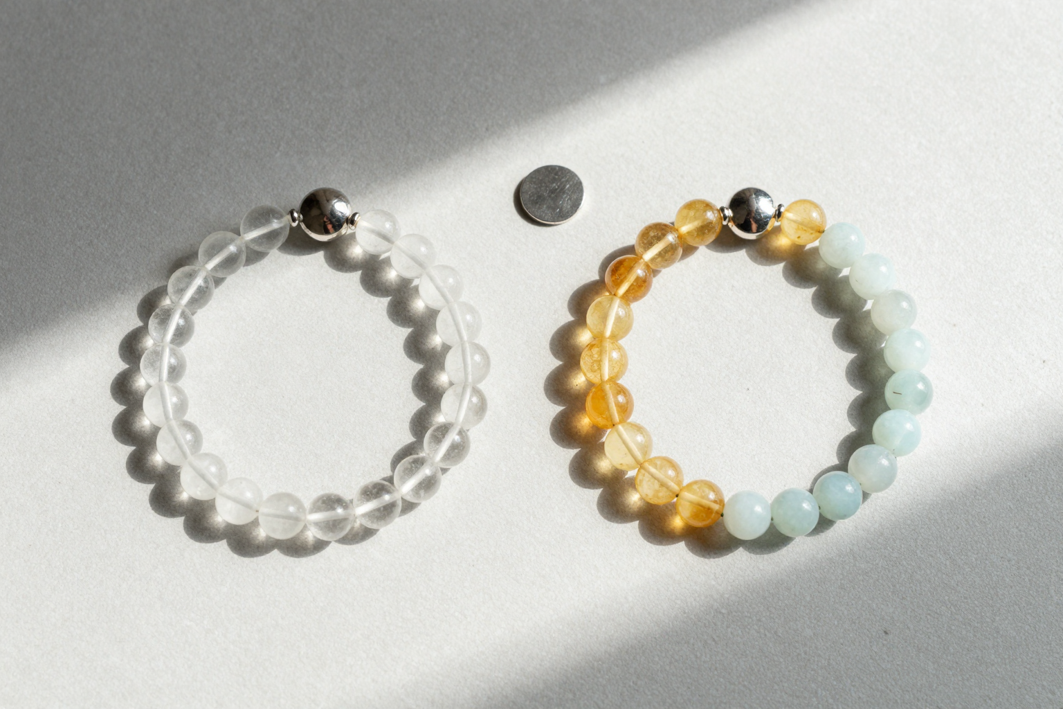 Clear quartz, citrine and blue lace agate bead bracelets mirrored on pale grey plaster with two silver discs and soft morning light